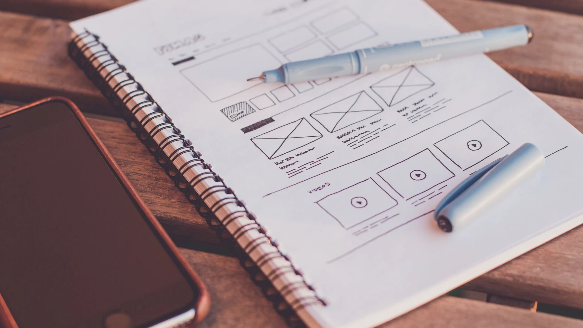 Graphic designer sketching mobile UI wireframes in a notebook during logo and brand discovery